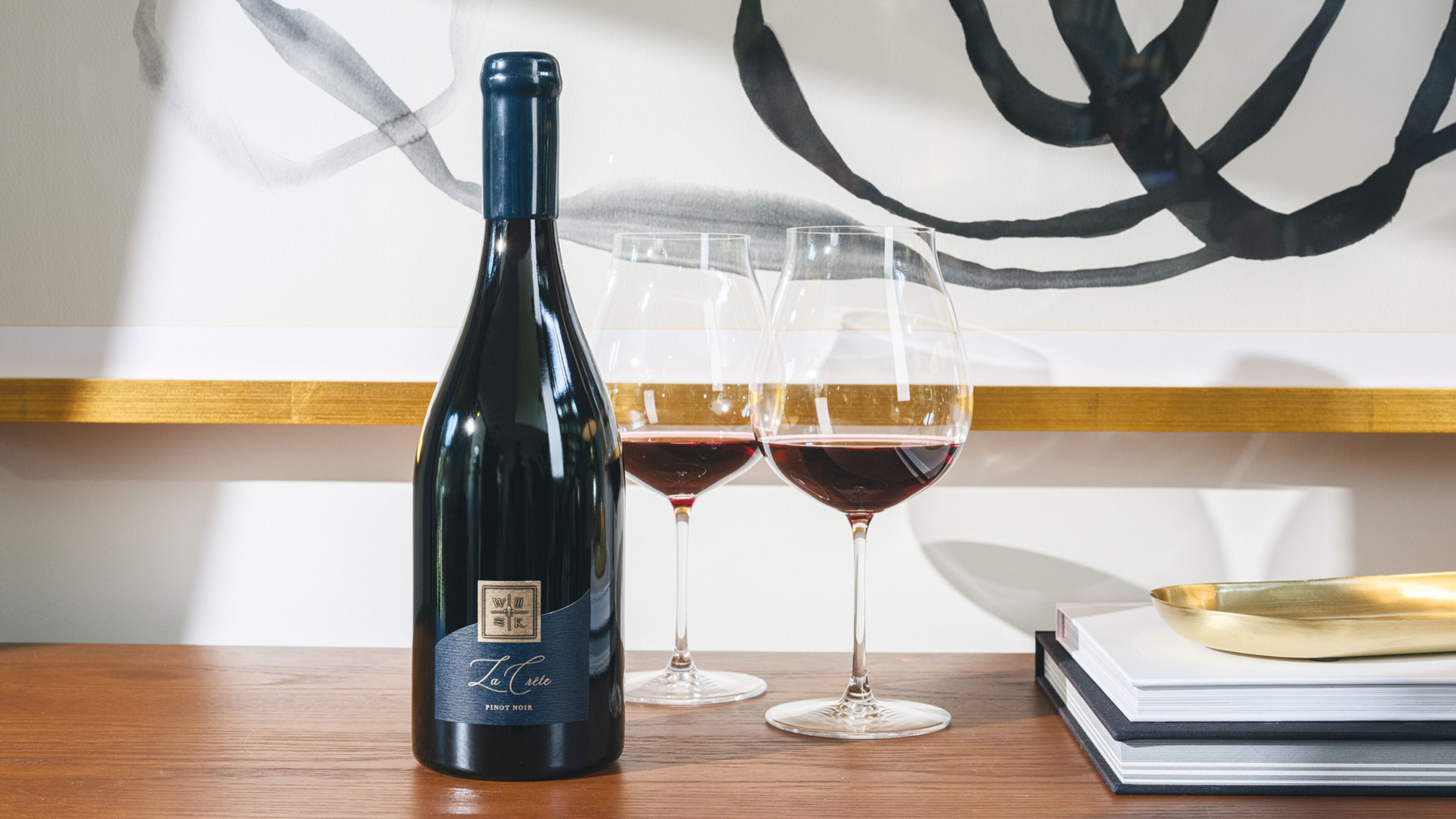 Bottle of La Crête Pinot Noir on armoire next to two glasses and books.